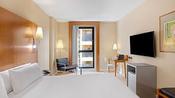 Ein Hotelzimmer mit einem großen Bett, einem Schreibtisch mit Stuhl, einem Fernseher und einem Fenster mit Blick ins Innere des Gebäudes.