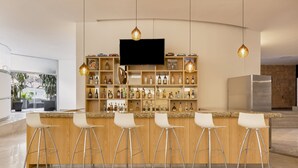 A modern bar area with a flat-screen TV, wooden shelves with bottles, and white bar stools. - Fiesta Inn Insurgentes Viaducto (Mexico City)