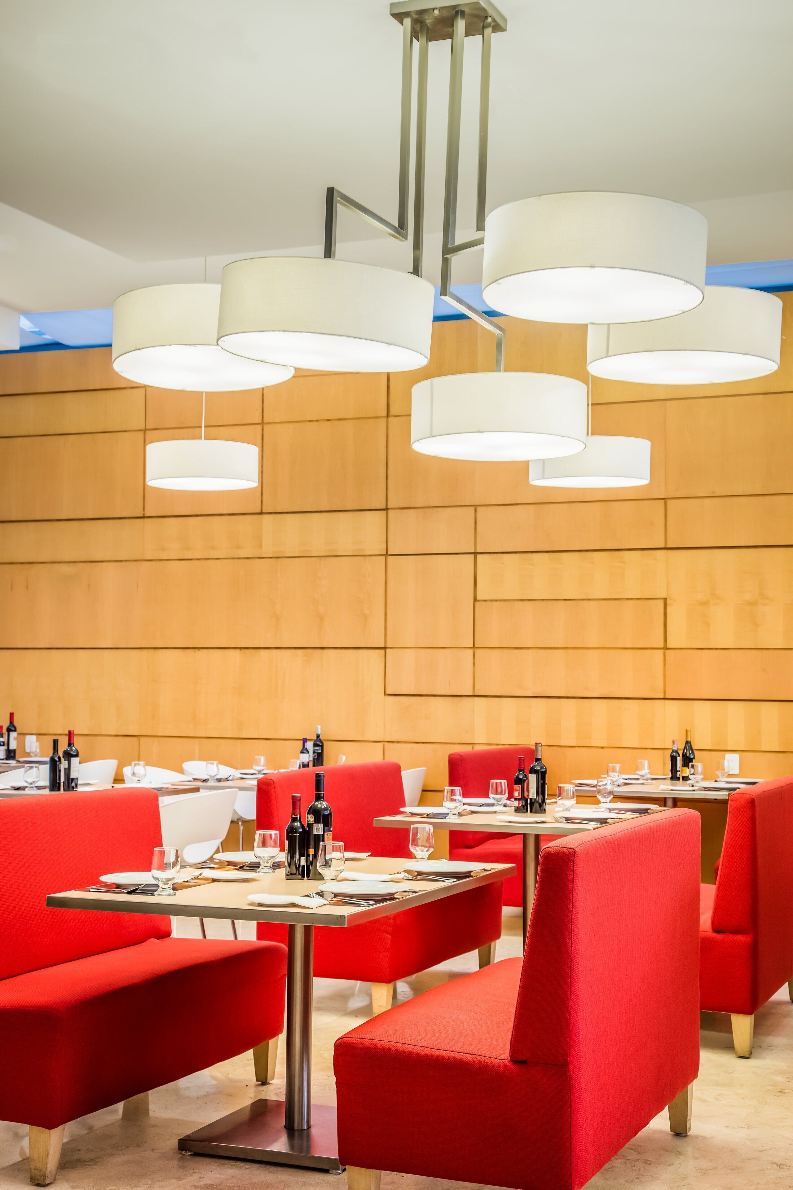 A restaurant with red upholstered booths and white pendant lighting. Tables are set with wine glasses and bottles.