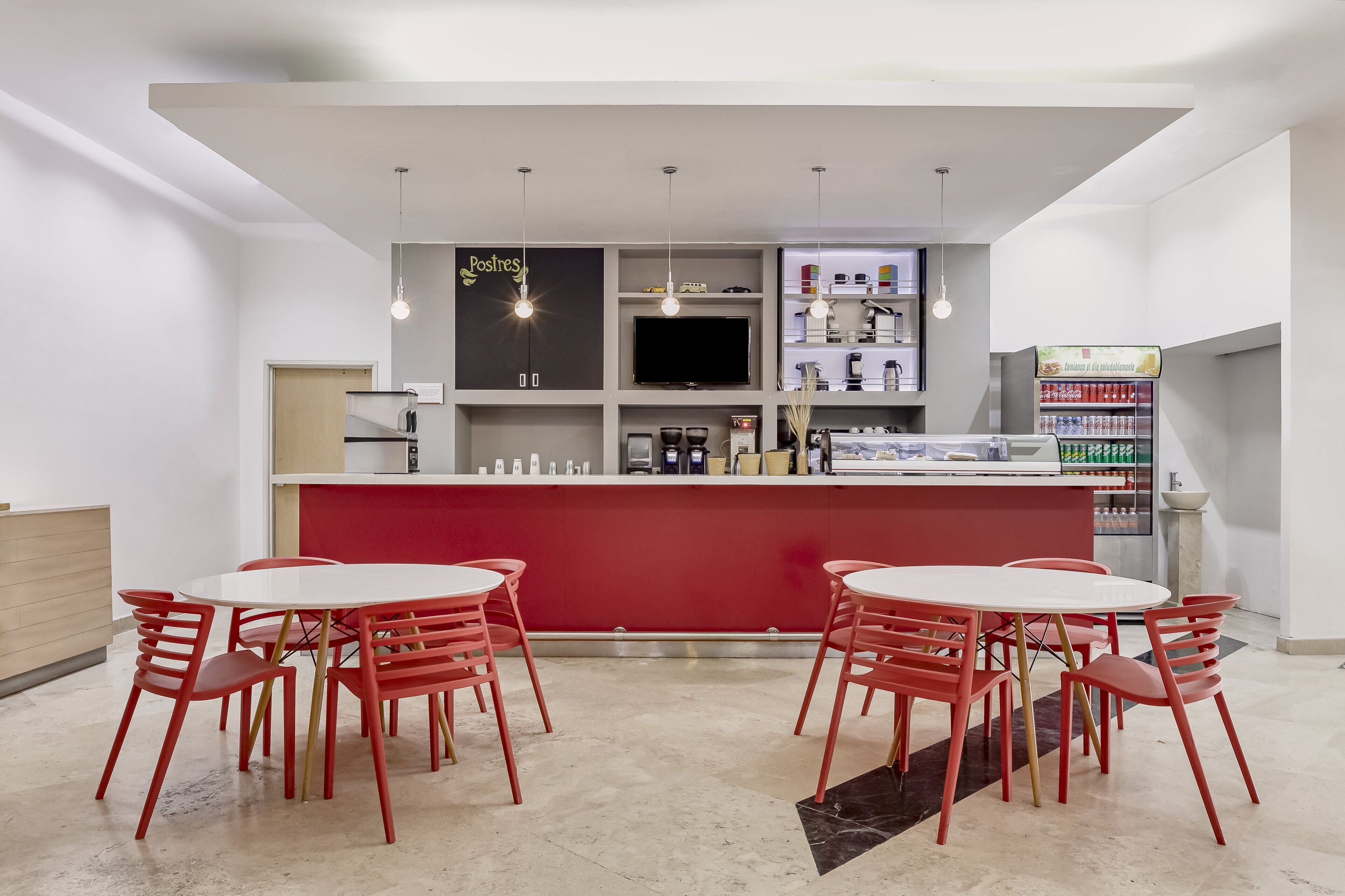 A modern bar area with red chairs and a white counter, featuring a television and various beverages.