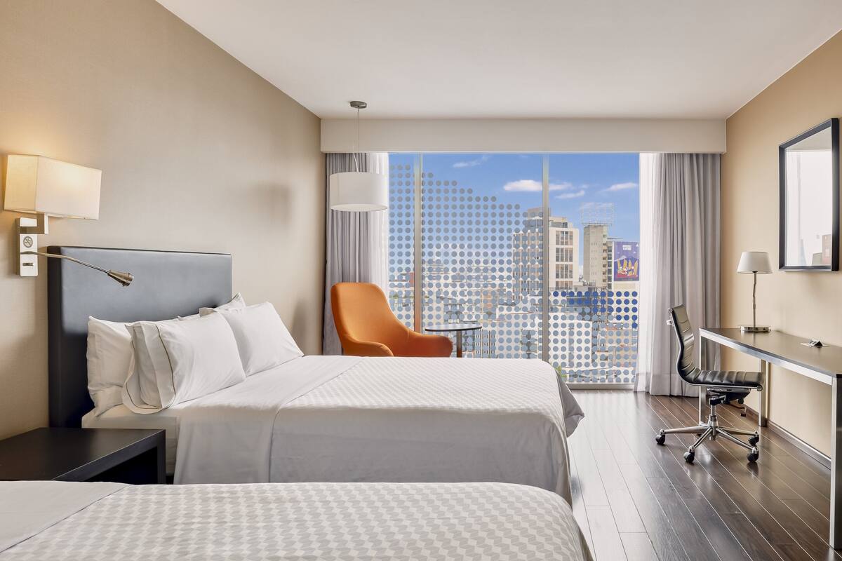 Habitación de hotel con una cama grande, un escritorio, una silla naranja y vistas a la ciudad.