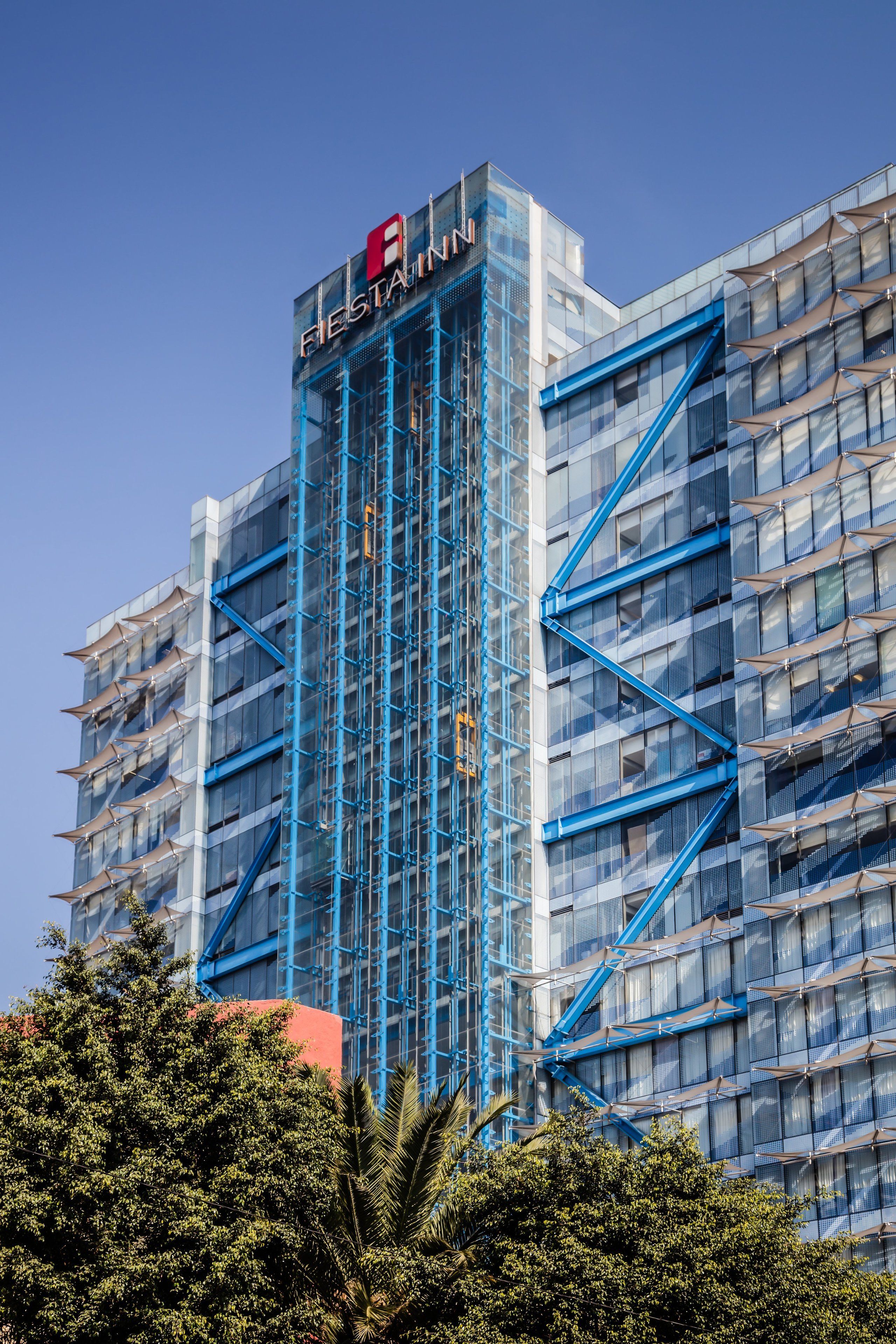 Un hôtel moderne, reconnaissable à son enseigne bien visible « Fleeting Inn », doté d’une façade en verre et d’éléments structurels bleus.