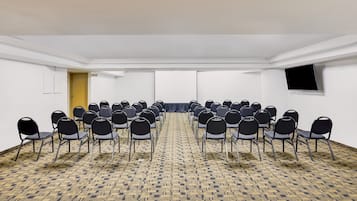 A conference room with rows of chairs, a carpeted floor, a door, and a flat-screen TV on the wall.