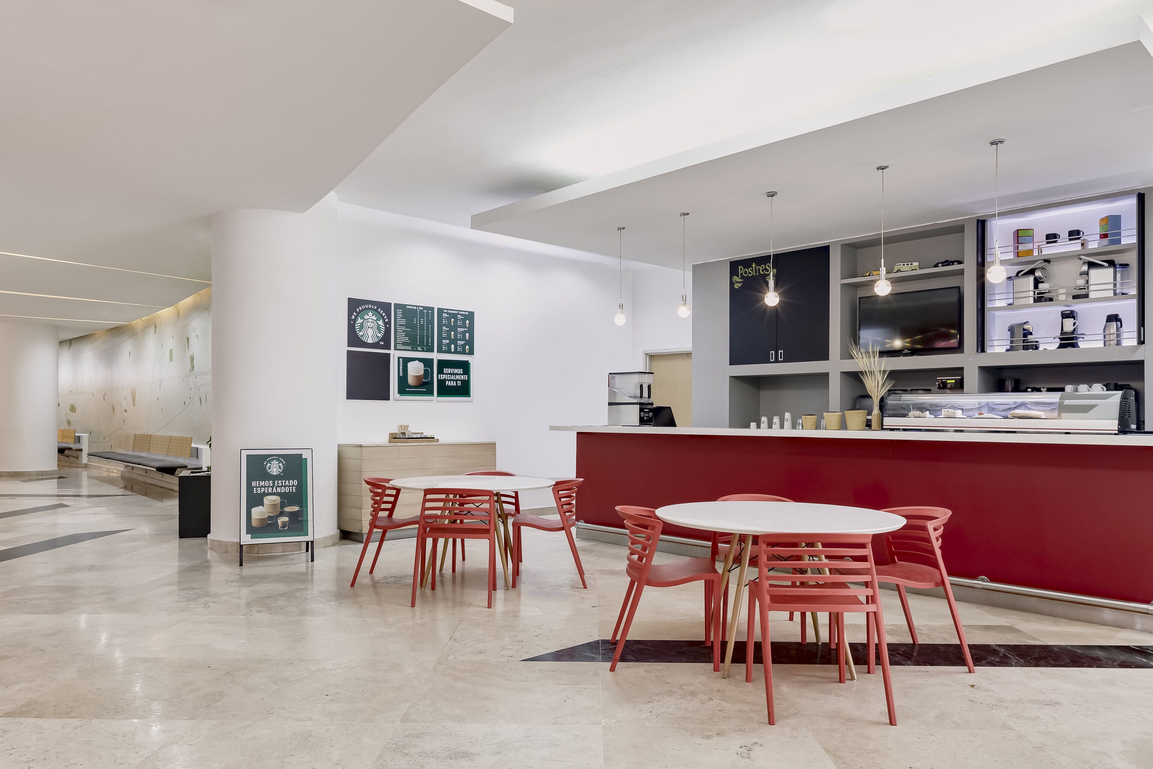 Una cafetería moderna con un mostrador rojo, mesas blancas y sillas rojas. Hay carteles de menú en la pared y un letrero de Starbucks.