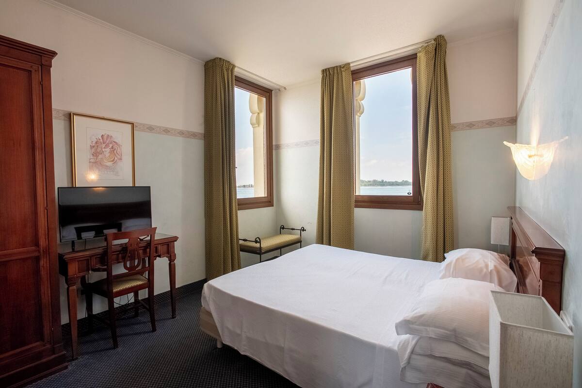 A hotel room with a bed, desk, chair, and a television.