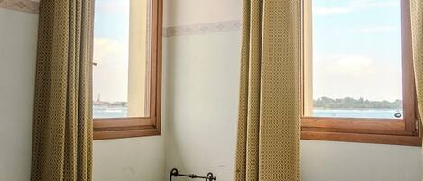 A room with a bed, a bench, and two windows with curtains.