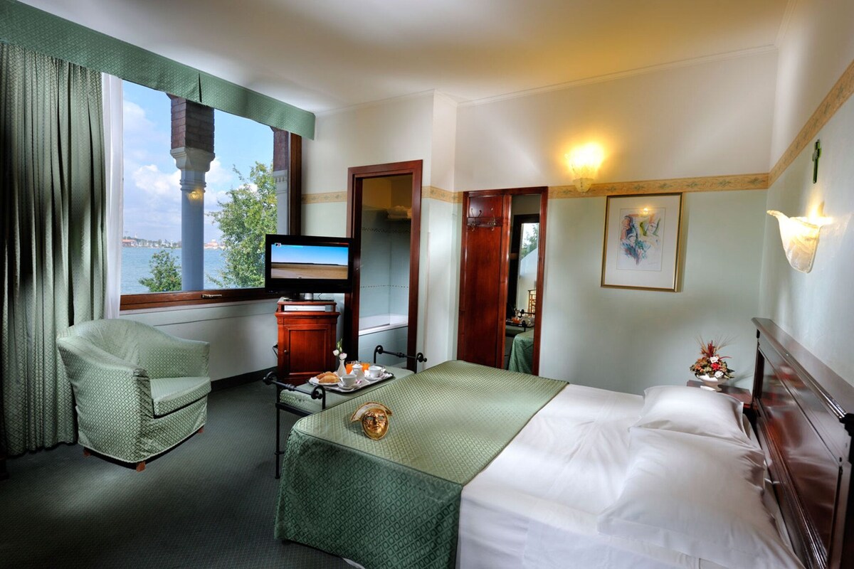Une chambre d’hôtel comprenant un lit, un bureau avec une télévision, une chaise et une fenêtre donnant sur un plan d’eau.