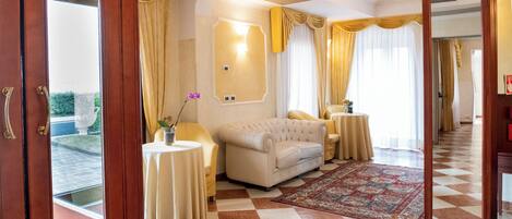 A hotel room with a checkered floor, a sofa, a round table, and a mirror.