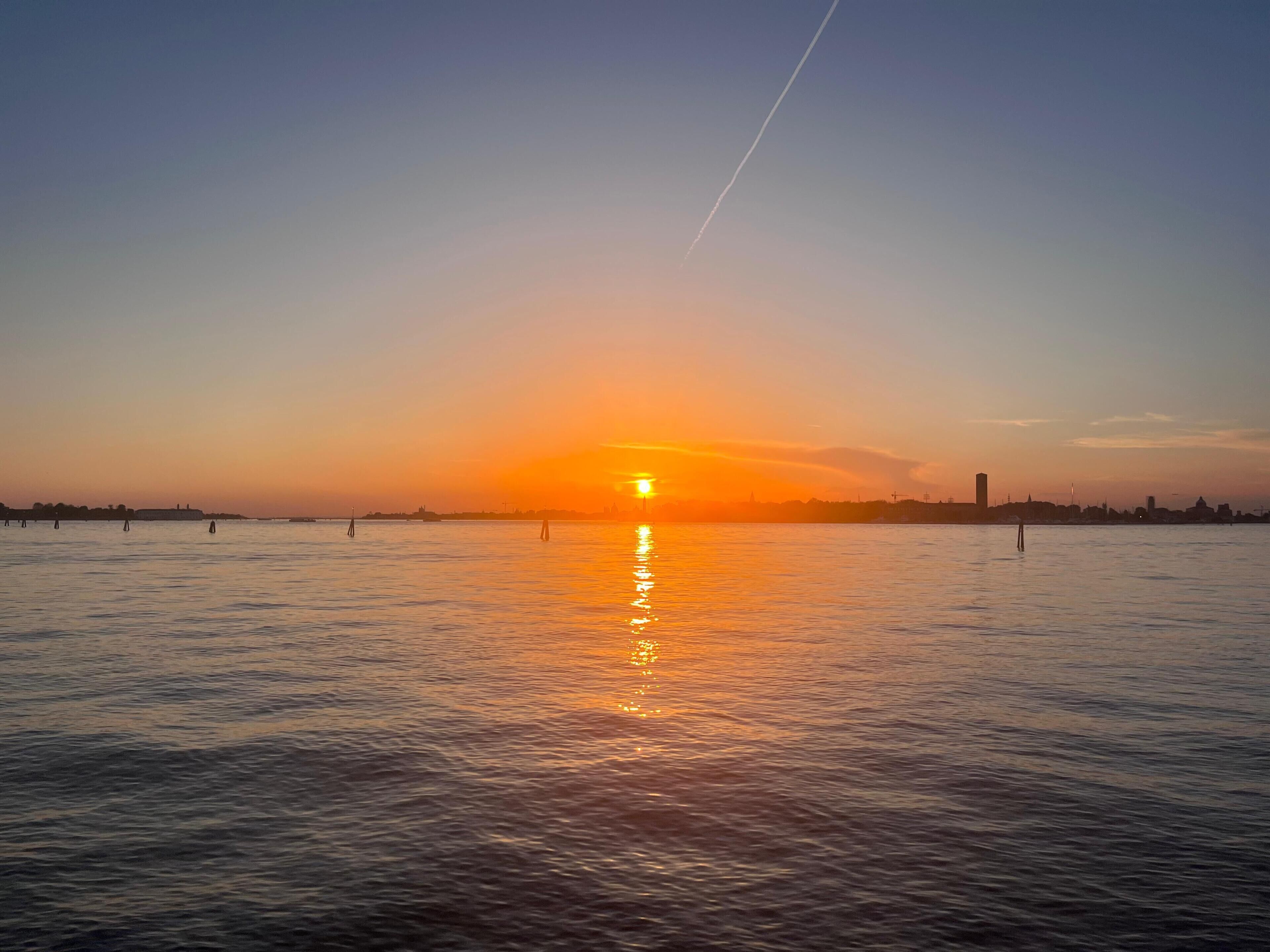 Un atardecer sobre un cuerpo de agua tranquilo con el horizonte de una ciudad a lo lejos.