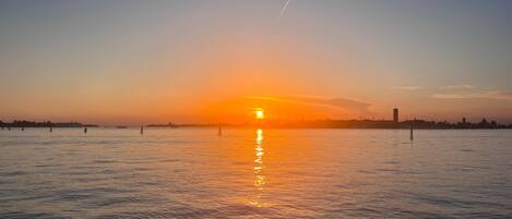 Un atardecer sobre un cuerpo de agua tranquilo con el horizonte de una ciudad a lo lejos.