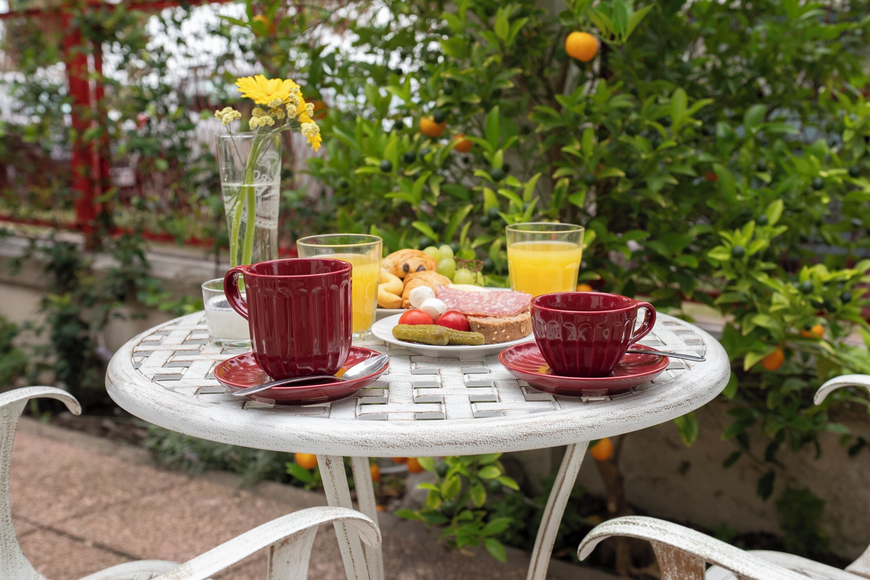 A round table with a white metal frame, red cups, a glass of orange juice, and a plate with food.