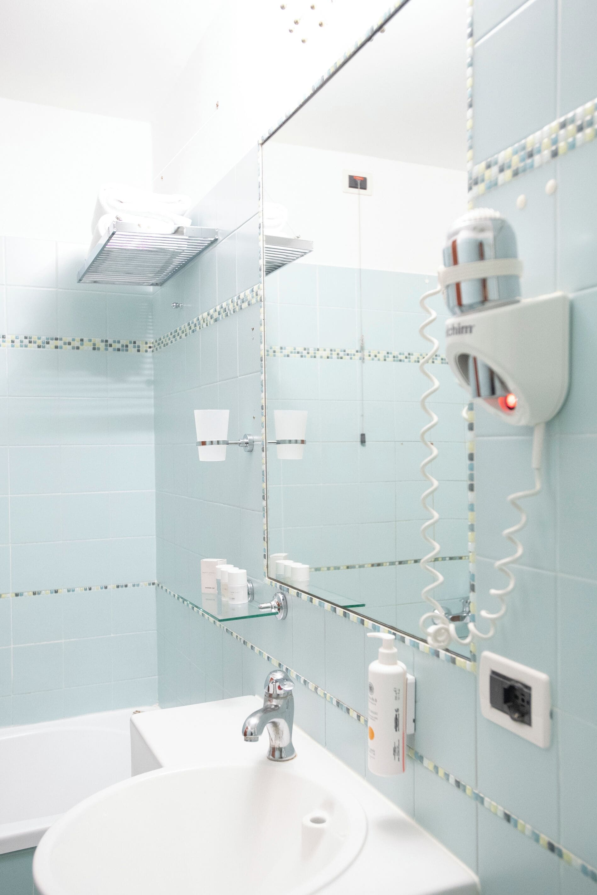 A bathroom with a white sink, a mirror, and a hairdryer mounted on the wall.