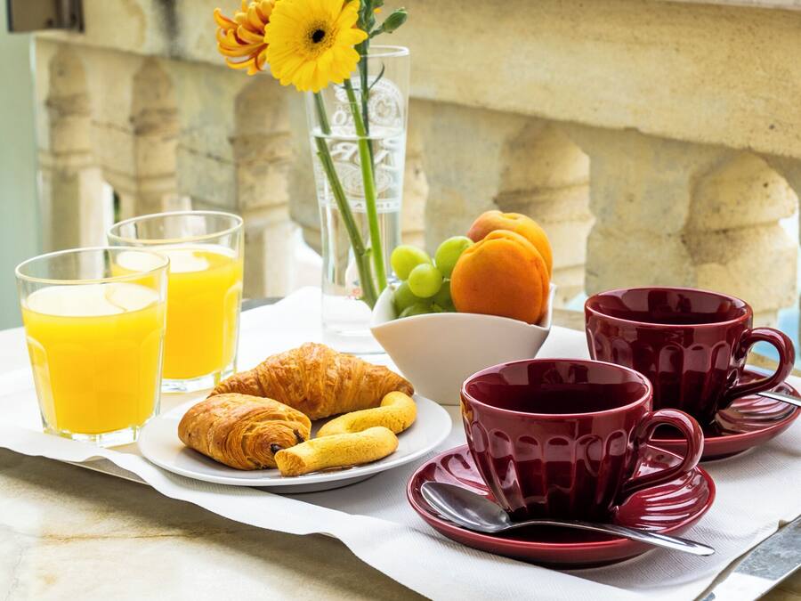 Un petit-déjeuner composé de croissants, de fruits et de jus d’orange, servi sur un balcon donnant sur une vue panoramique de la ville.
