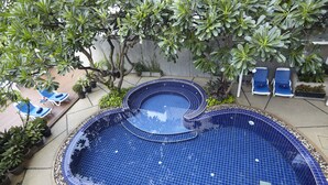 Ein Swimmingpool mit blau gefliestem Innenraum, umgeben von Kübelpflanzen und zwei Liegestühlen.
