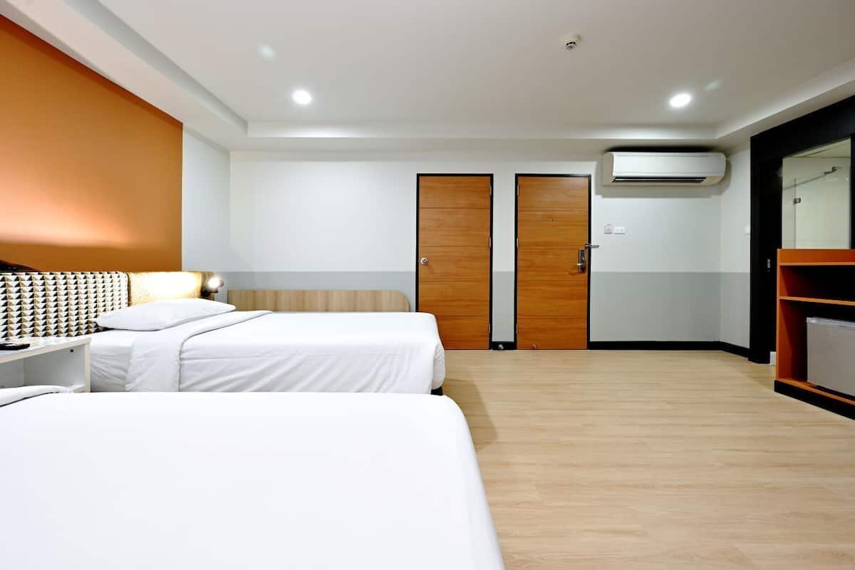Une chambre d’hôtel avec deux lits, une tête de lit en bois, un appareil de climatisation et une armoire.