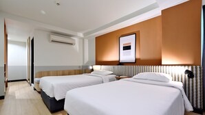 Ein Hotelzimmer mit zwei Betten, einem großen Fenster, einer Klimaanlage und einem gerahmten Bild an der Wand.