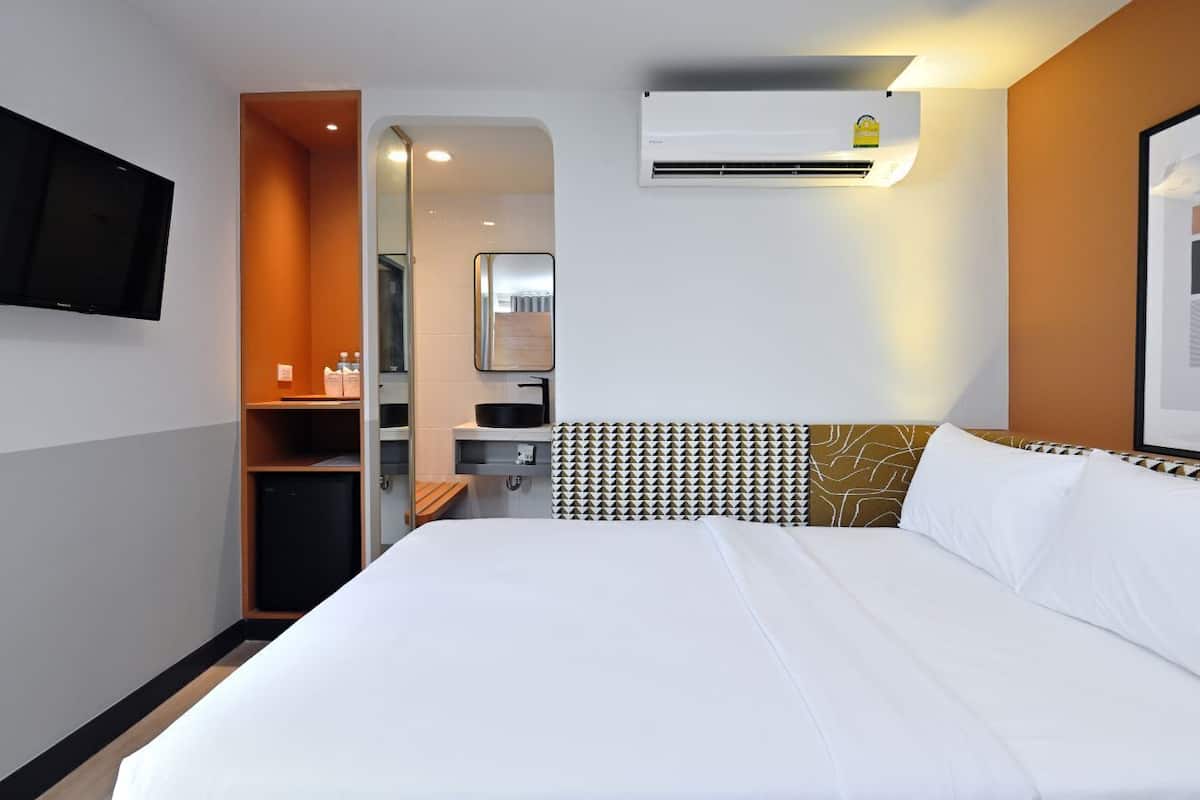 Une chambre d’hôtel équipée d’un lit, d’un téléviseur fixé au mur, d’un système de climatisation intégré et d’un petit coin cuisine.