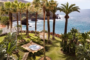 Un jardin tropical agrémenté de palmiers et doté d’un jacuzzi, offrant une vue sur une côte rocheuse.