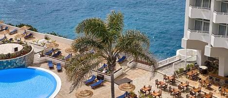 A resort with a pool area, lounge chairs, and a view of the ocean.