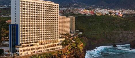 A multi-story hotel with a coastal view, situated on a cliff overlooking the ocean.