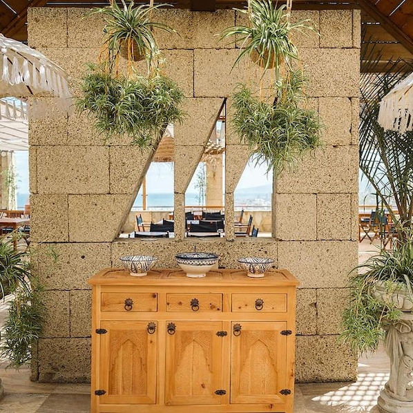 Un mueble de madera con tiradores decorativos, una pared de piedra y plantas en macetas.