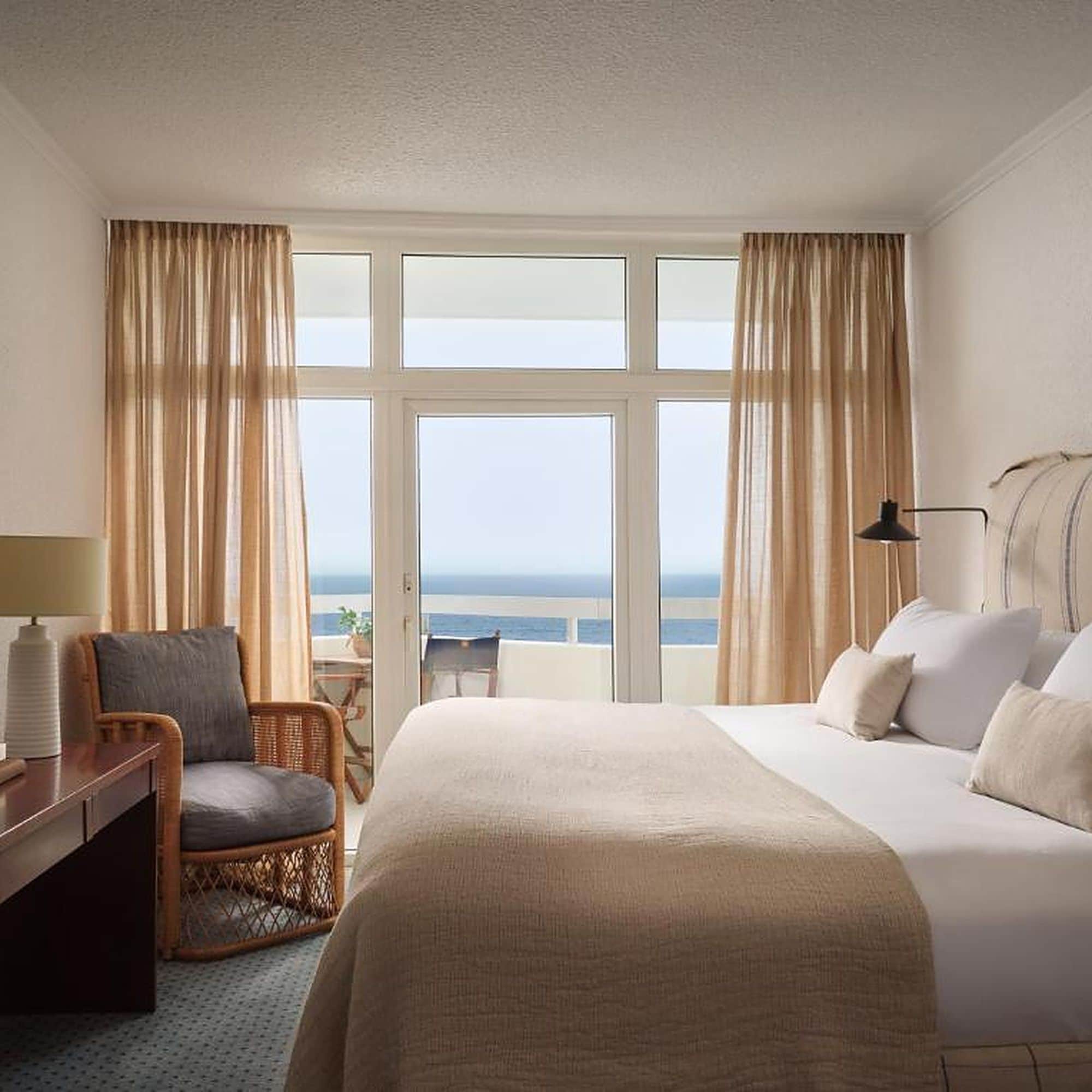 Una habitación de hotel con una cama, una silla, un escritorio y vista al mar.