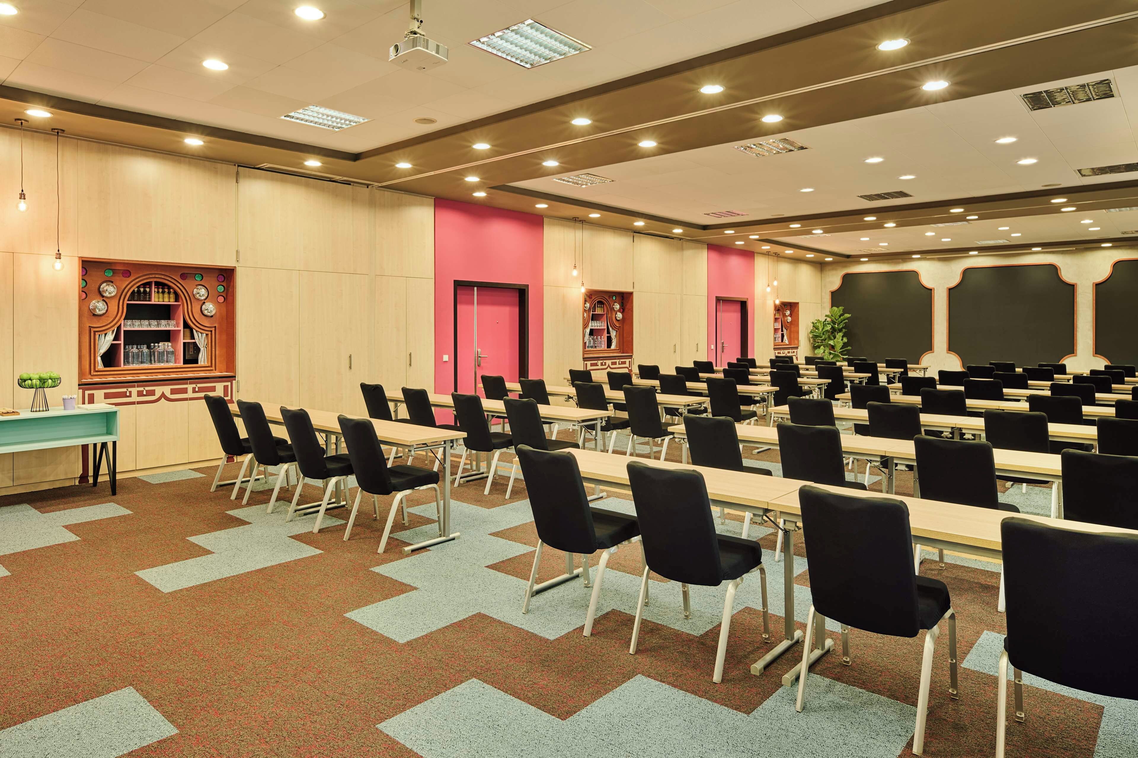 Ein Konferenzraum mit Tischen und Stühlen, einem Projektor und einer großen Leinwand.