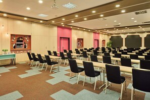 Un salón de conferencias con filas de mesas y sillas, un proyector y una pantalla grande.