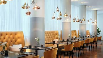 A modern dining area with a long table, multiple chairs, and hanging pendant lights.