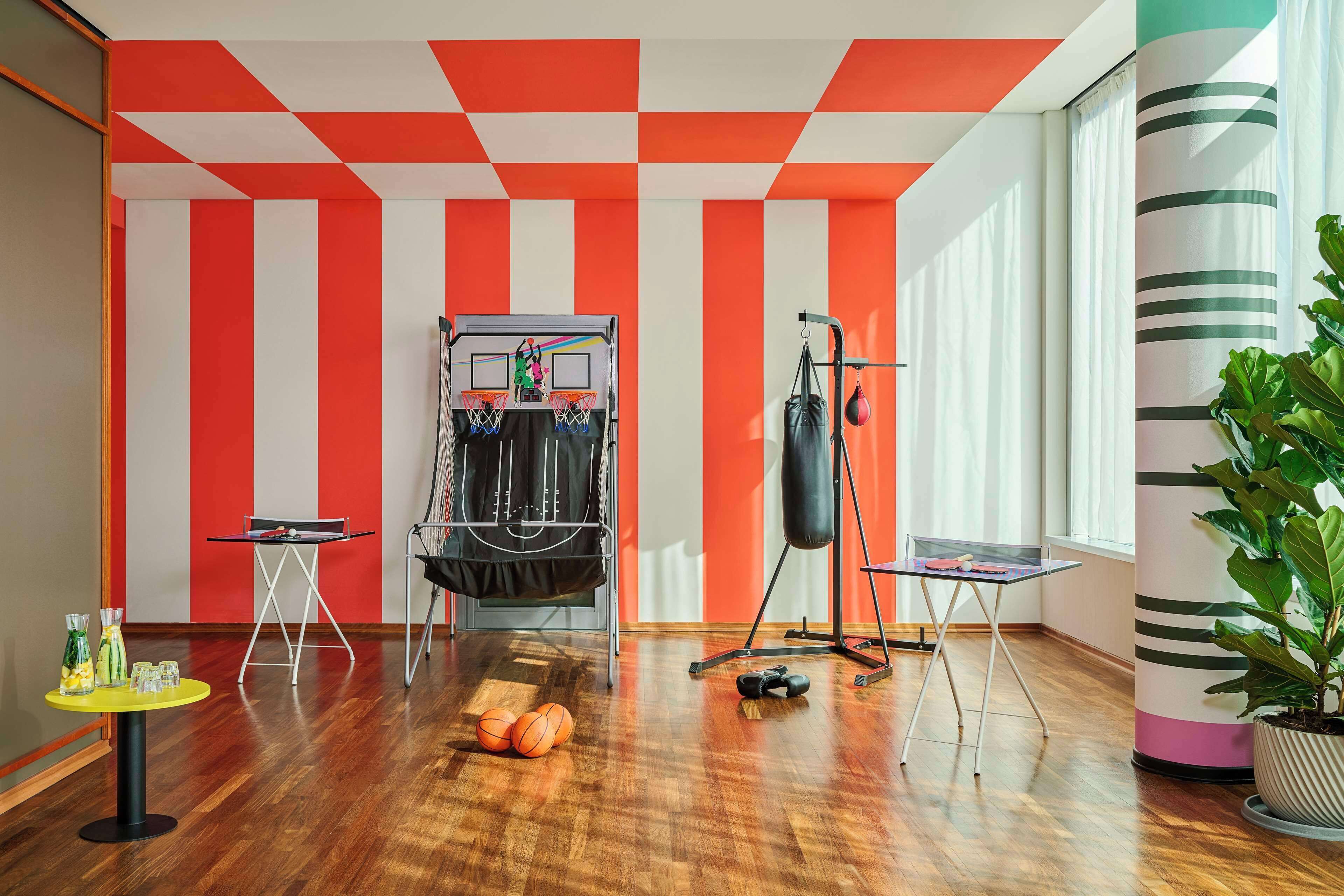 Una habitación con suelo de madera, un saco de boxeo, una mesa con una silla y un aro de baloncesto.