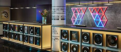 Un área de recepción moderna con una exhibición de discos de vinilo, un pilar con un reloj y luces de neón geométricas.