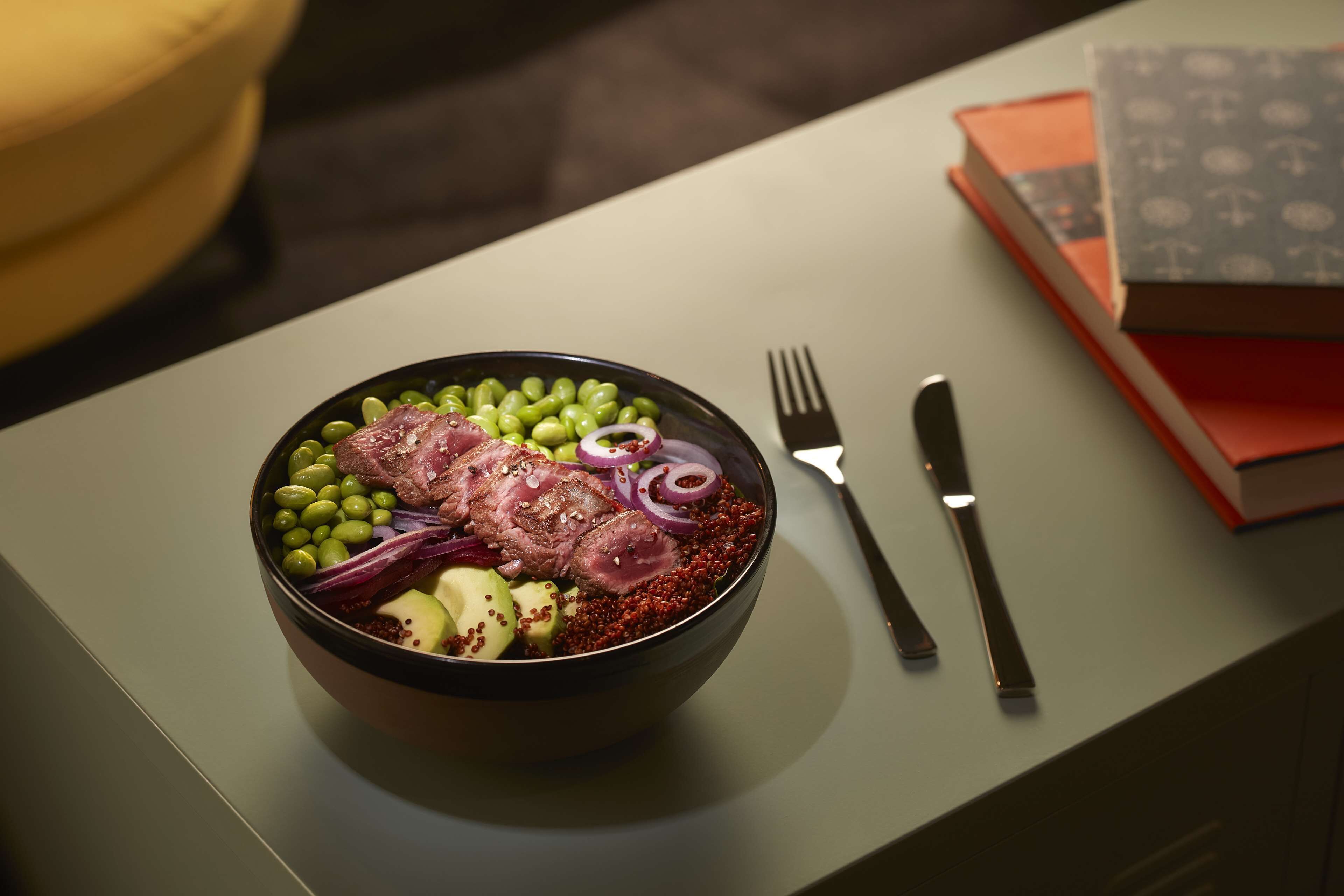 A bowl of food on a table with a fork and knife beside it.