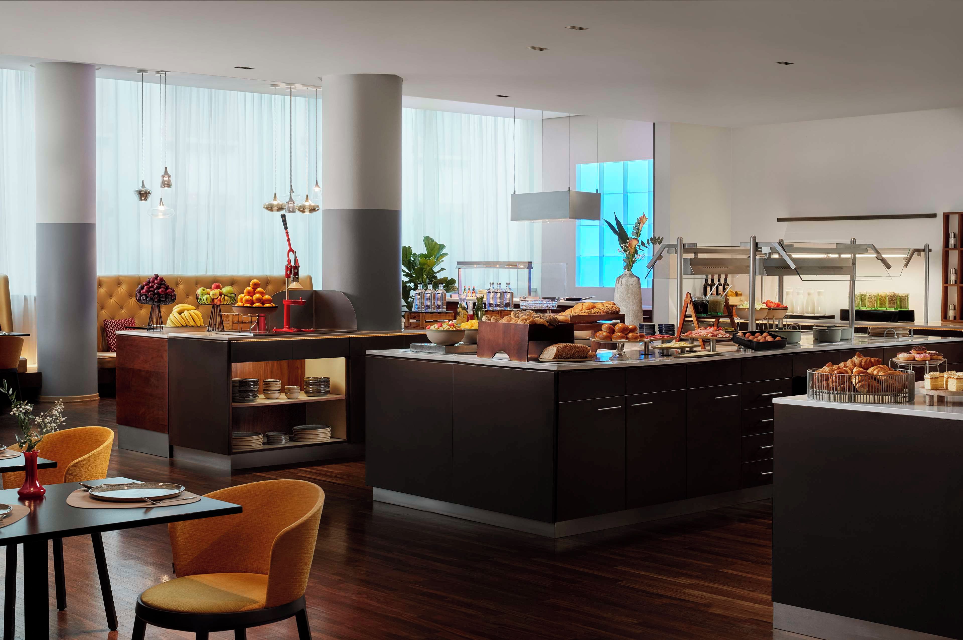 Un comedor de hotel moderno con una isla central, asientos y una barra de buffet.