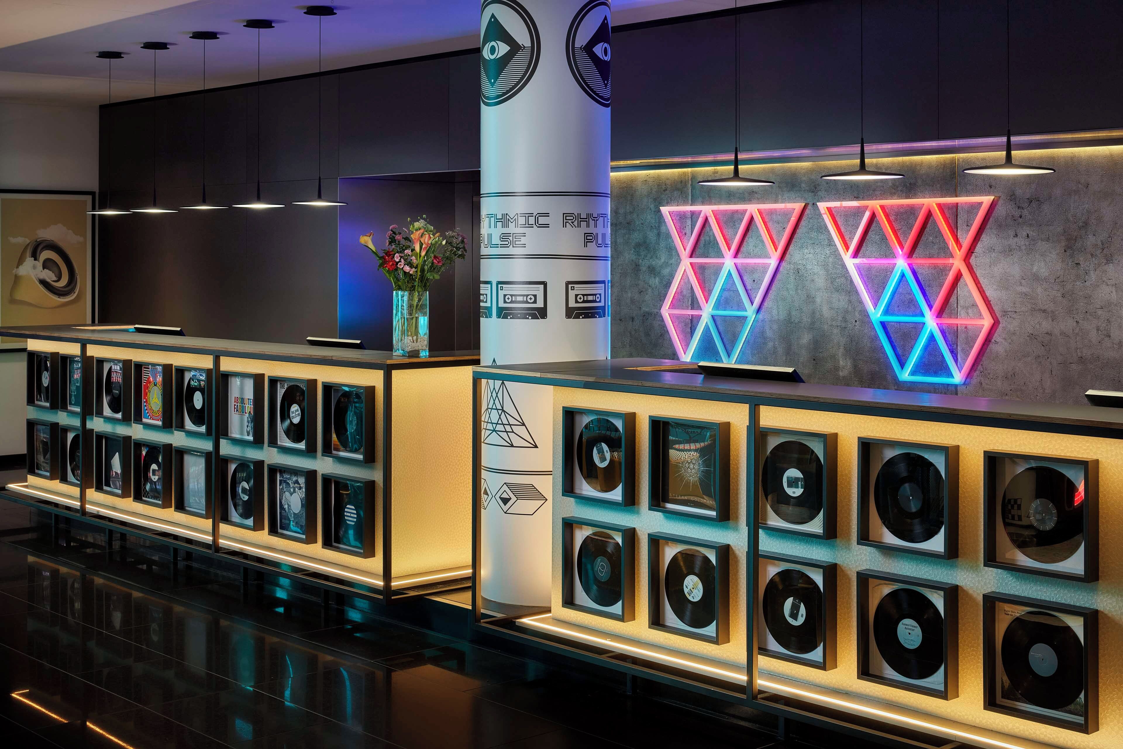 Un área de recepción moderna con una exhibición de discos de vinilo e iluminación neón geométrica.