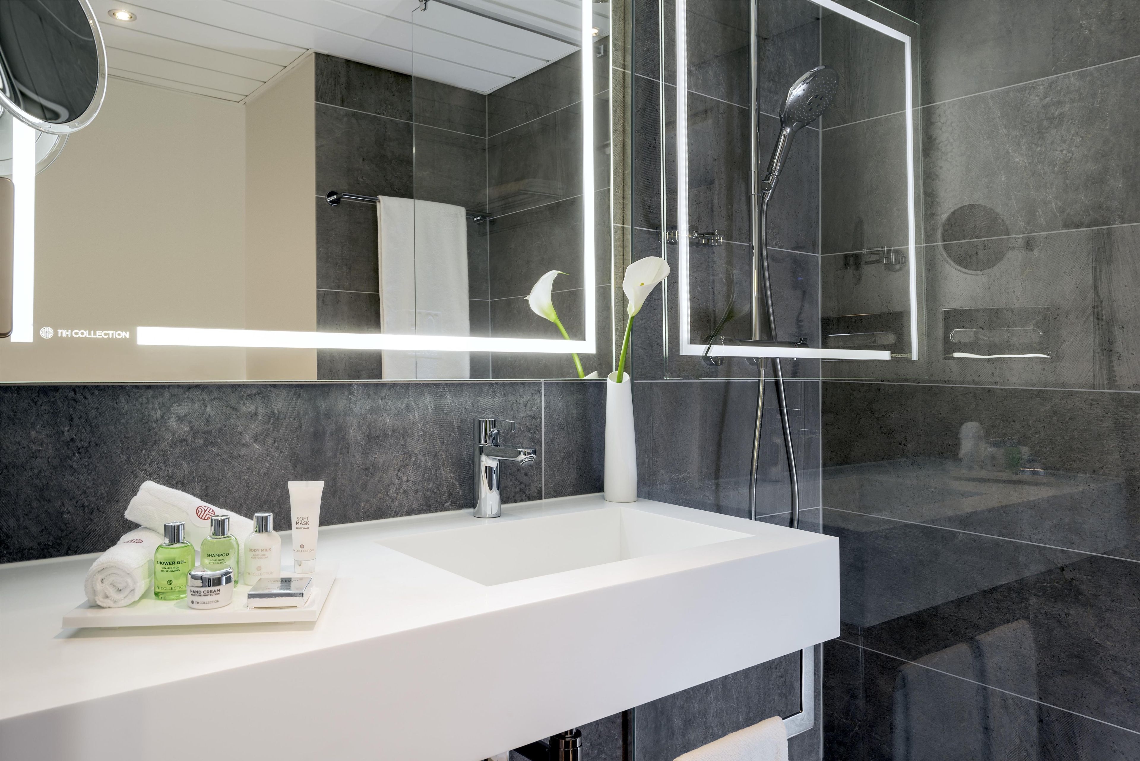 Une salle de bain moderne avec un lavabo blanc, une douche à parois de verre et un grand miroir.