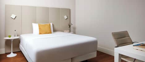 Una habitación de hotel con una cama, una mesita de noche, una silla, un escritorio y un reloj.