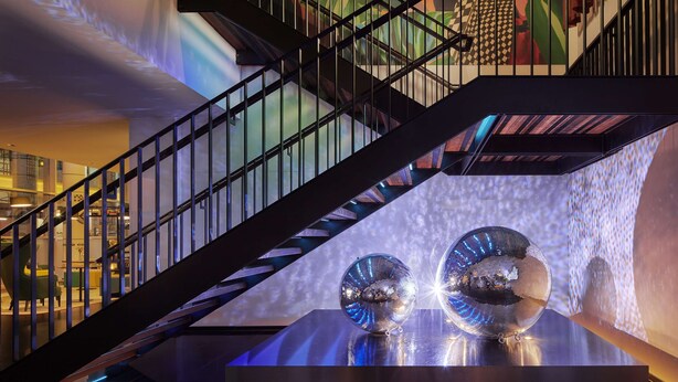 Un escalier moderne avec une rampe en métal et une boule à facettes réfléchissante sur une plateforme.