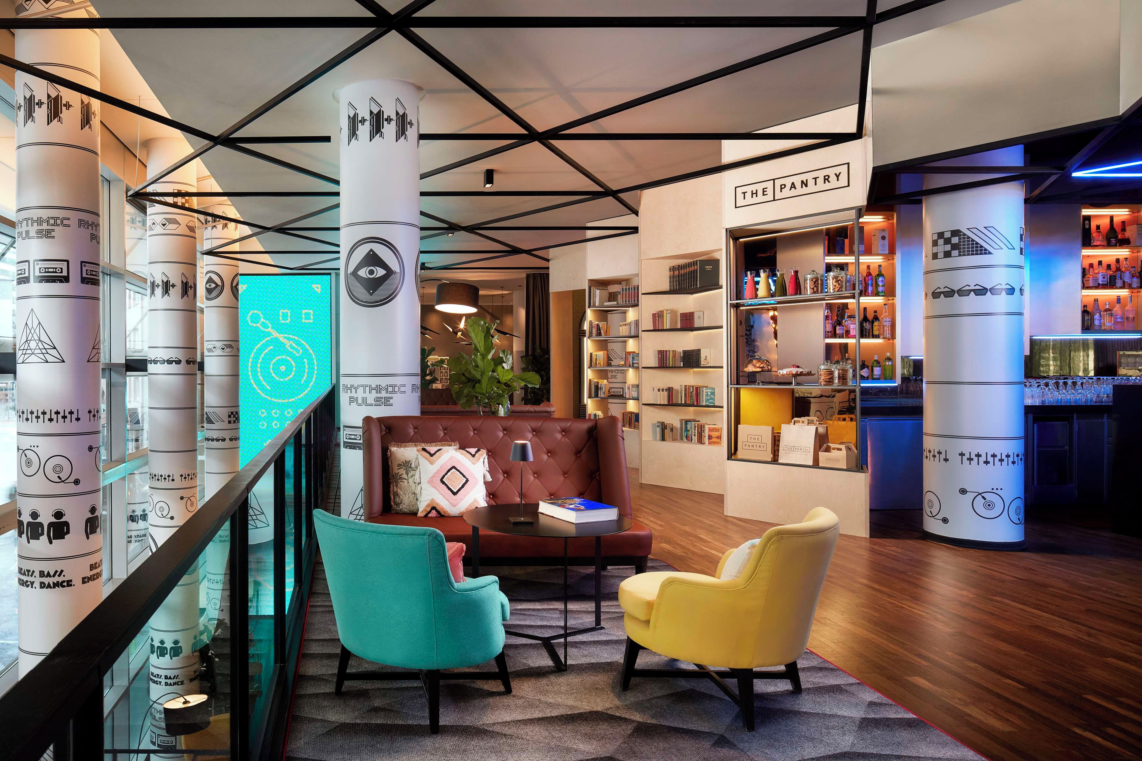 Un lobby moderno con una zona de estar central, una estantería y un bar con la leyenda 'THE PANTRY'.