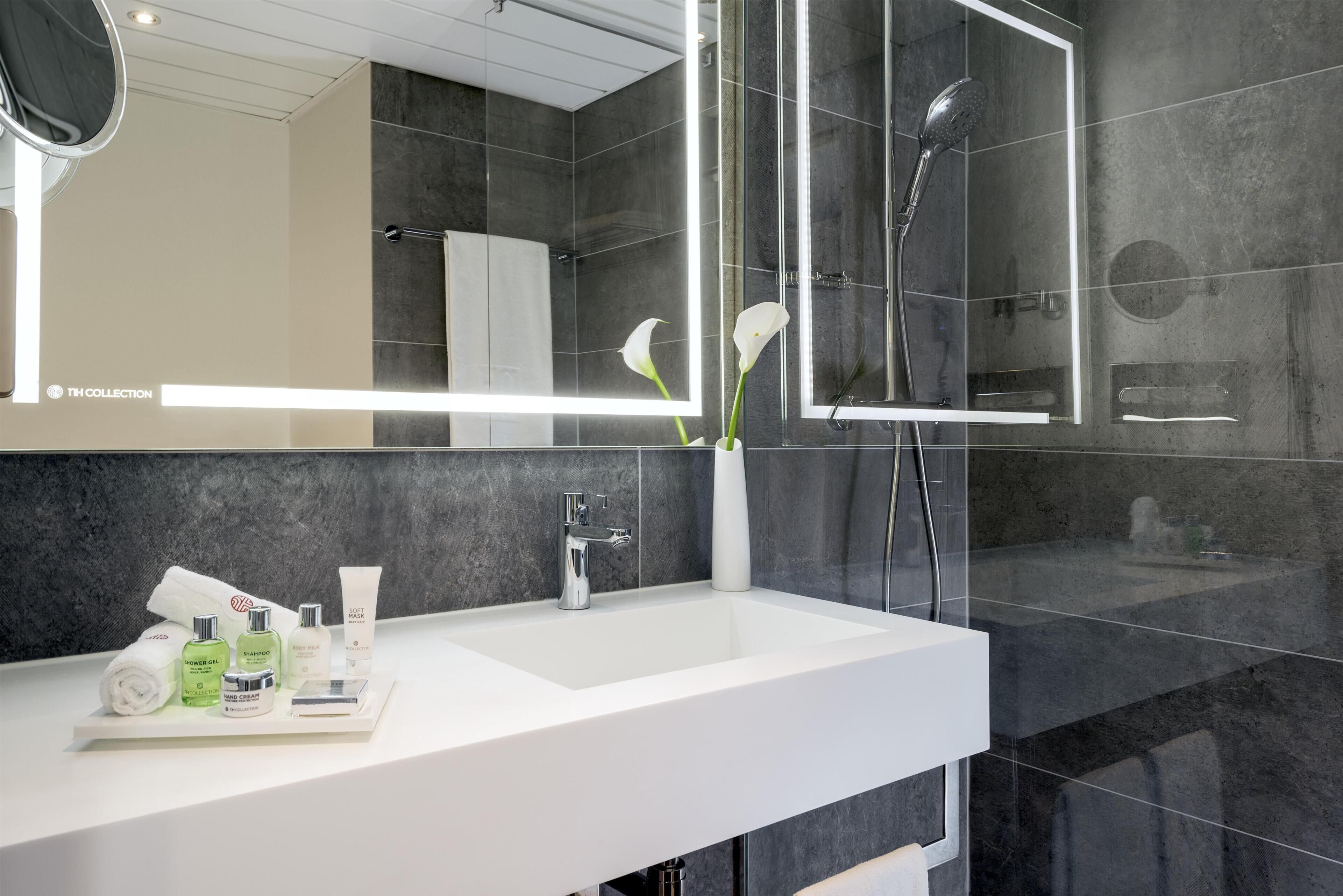 A modern bathroom with a white sink, a glass shower enclosure, and a large mirror.