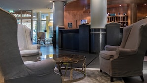 A lobby with a reception desk, two armchairs, a glass coffee table, and a reception area with a wooden wall and a sign. - Congress Hotel Weimar by Mercure (Weimar)