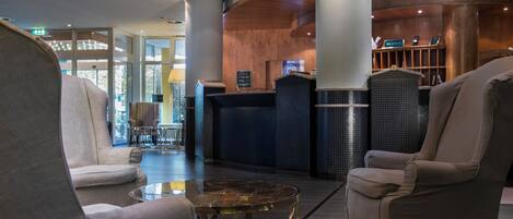 Un hall d’entrée avec un comptoir de réception, deux fauteuils, une table basse en verre et un espace d’accueil agrémenté d’un mur en bois et d’une enseigne.