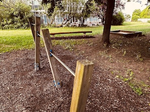 Children can play on the seesaw and swing set in this outdoor play area surrounded by trees and a building.