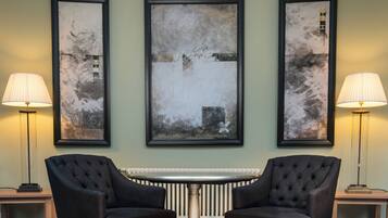 Une pièce dans laquelle on trouve trois tableaux abstraits encadrés accrochés au mur, deux fauteuils noirs, une table ronde et deux lampadaires.