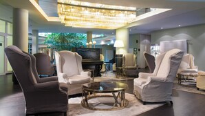A modern lounge area with a grand chandelier, comfortable seating, and a piano. - Congress Hotel Weimar by Mercure (Weimar)