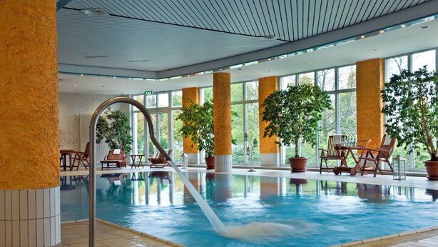 An indoor swimming pool with clear water, surrounded by potted plants and wooden chairs. - Congress Hotel Weimar by Mercure (Weimar)