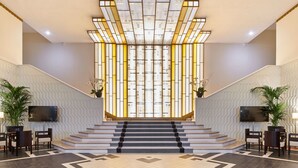 Un vaste hall d’entrée avec un escalier, un grand téléviseur fixé au mur et des plantes en pot.
