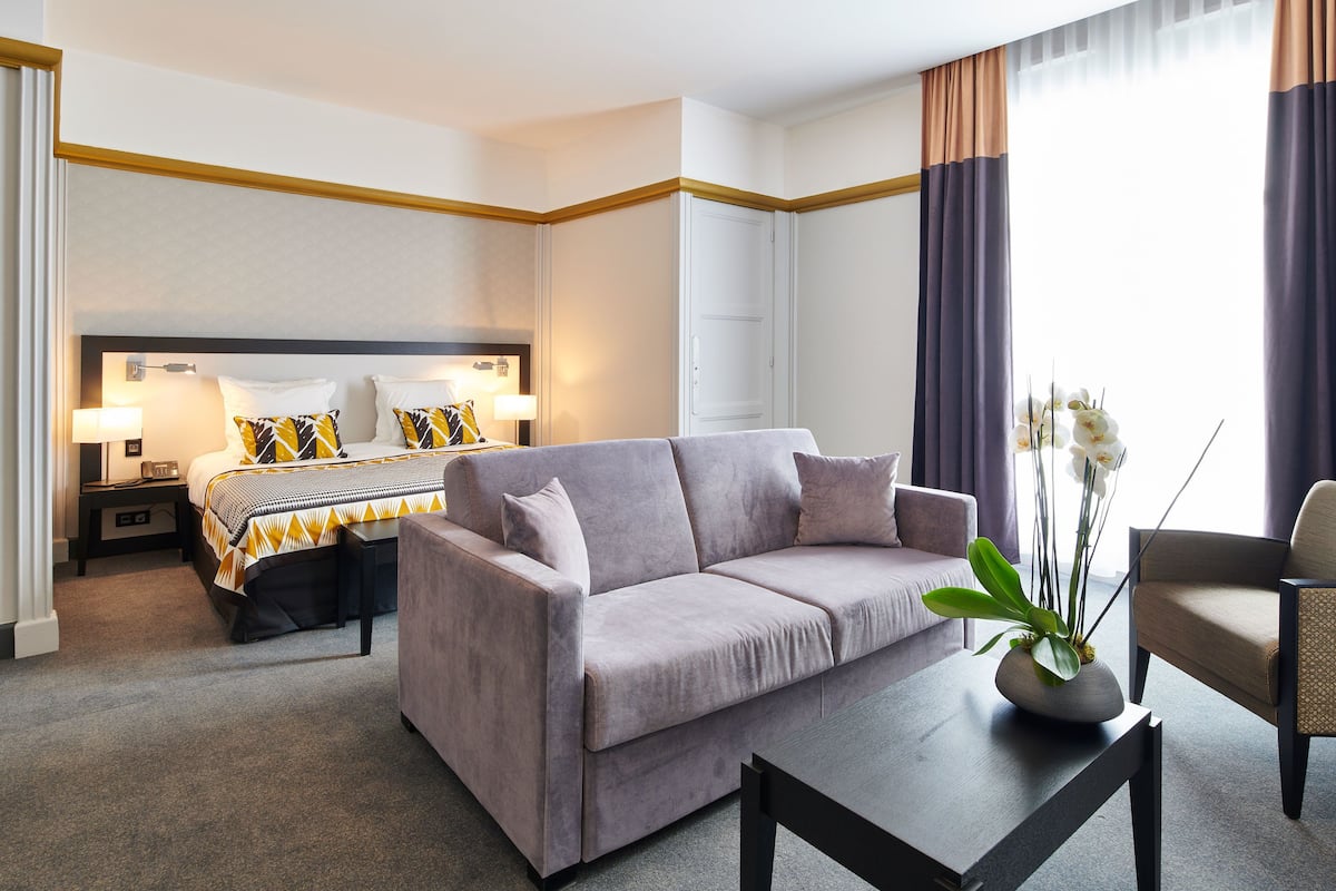 A hotel room with a bed, a sofa, a coffee table, and a chair.