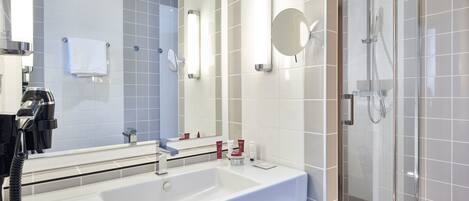 A modern bathroom with a large mirror, a sink, and a glass-enclosed shower.