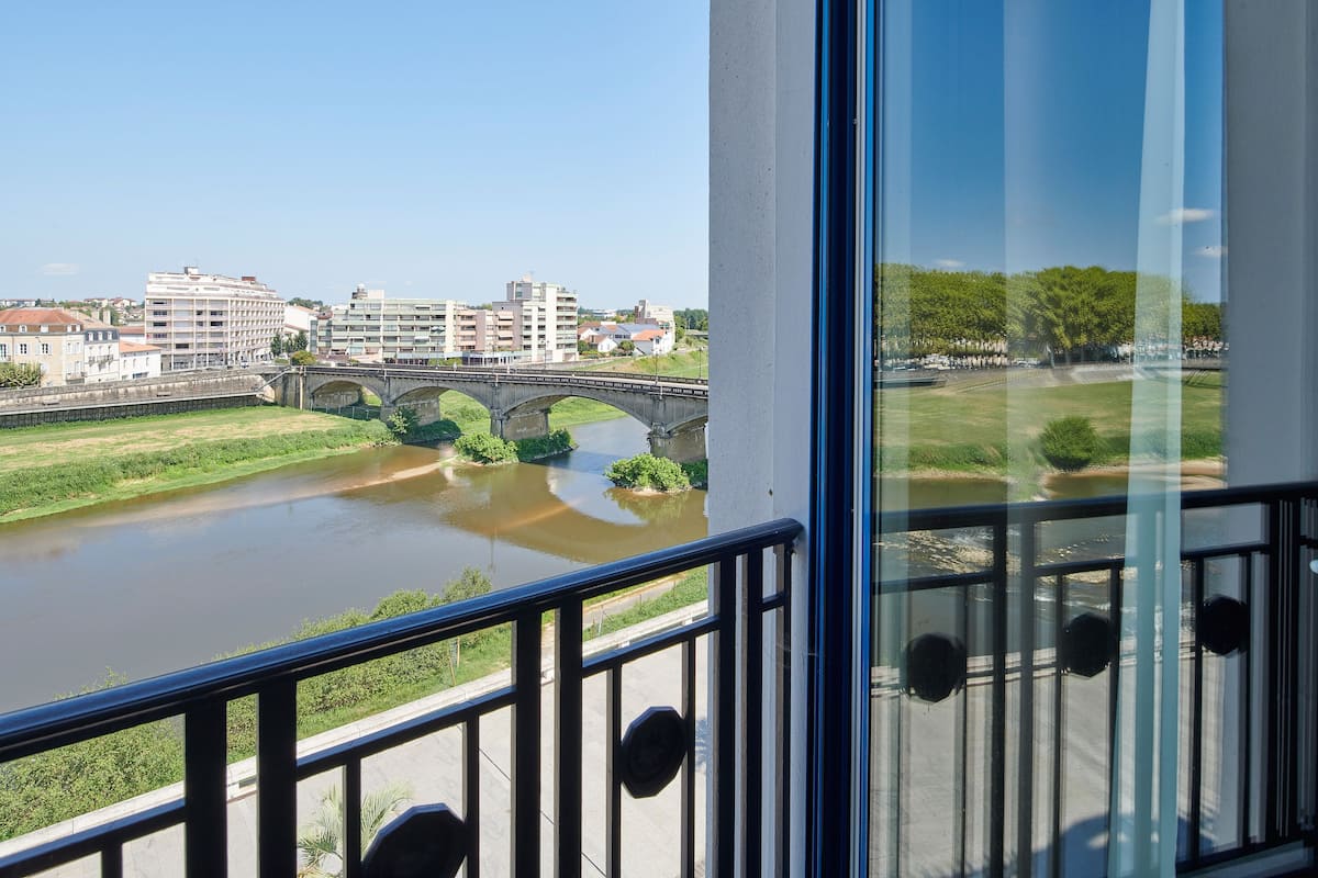 A balcony with a view of a river, a bridge, and buildings in the background.