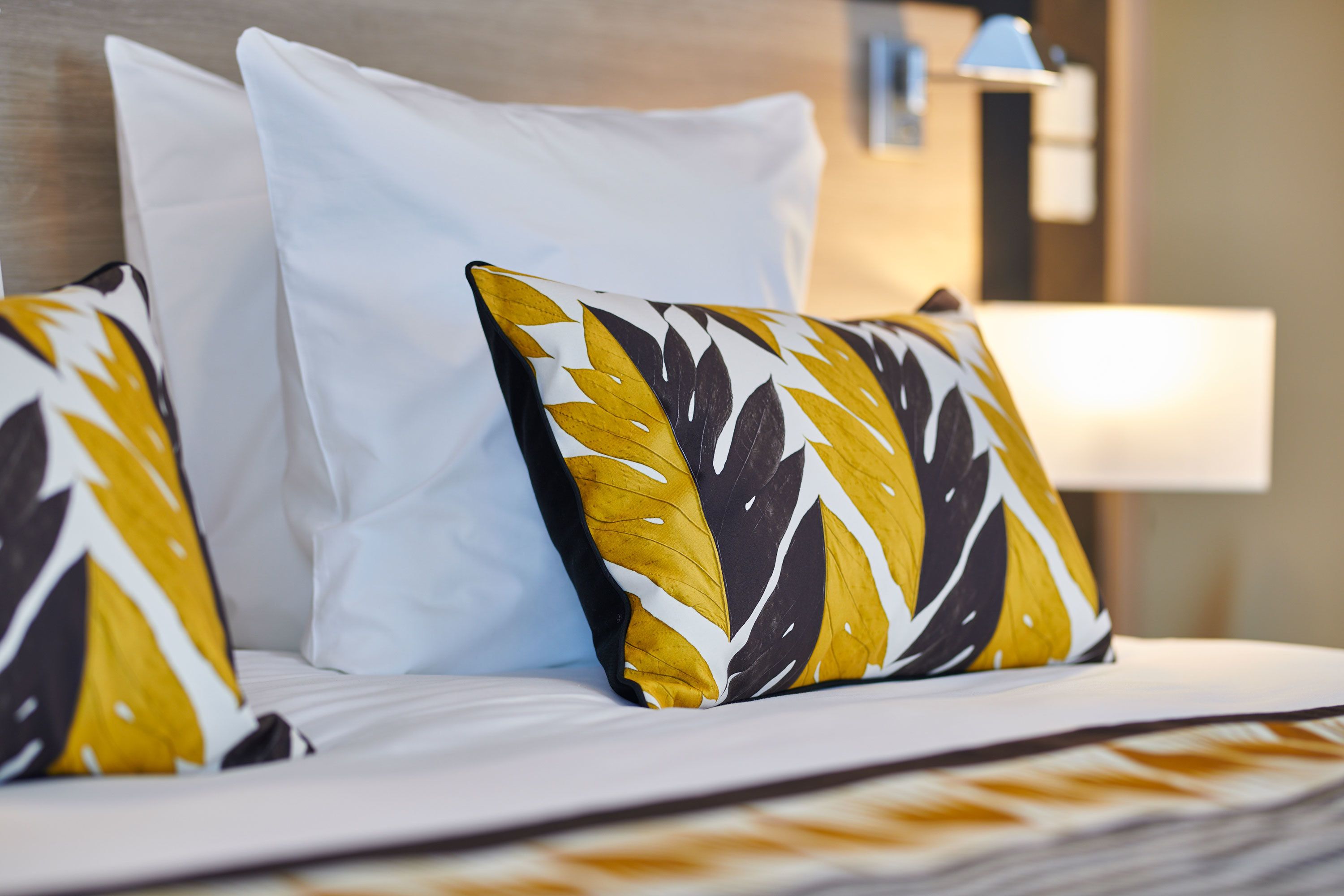 Una cama con almohadas blancas y estampadas, cabecera de madera y una lámpara de noche.
